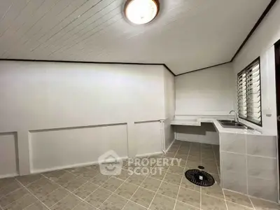 Spacious utility room with tiled flooring and sink, ideal for laundry or storage.