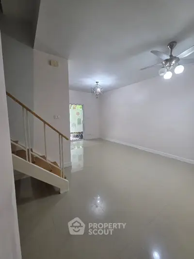 Spacious living room with modern lighting and staircase, perfect for family gatherings.