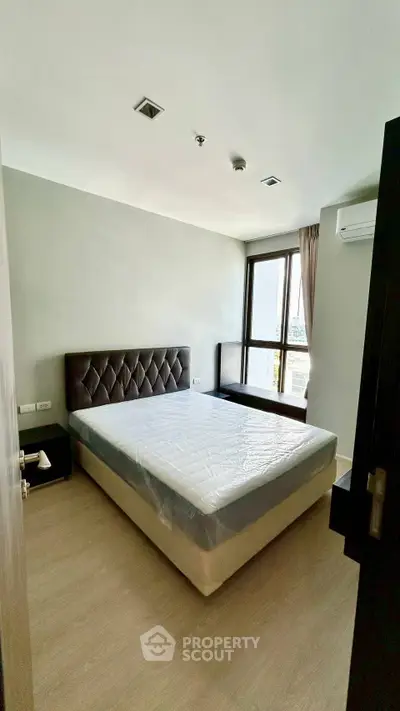 Modern bedroom with large window and minimalist design in a high-rise apartment.