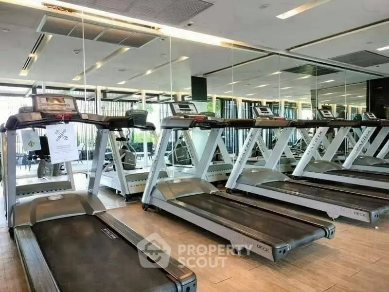 Modern gym with multiple treadmills and mirrored walls in luxury apartment building.