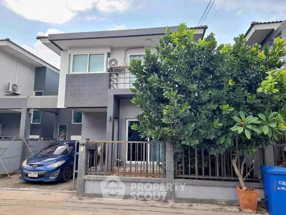 Modern two-story house with a car parked in driveway, lush tree, and sleek exterior design.