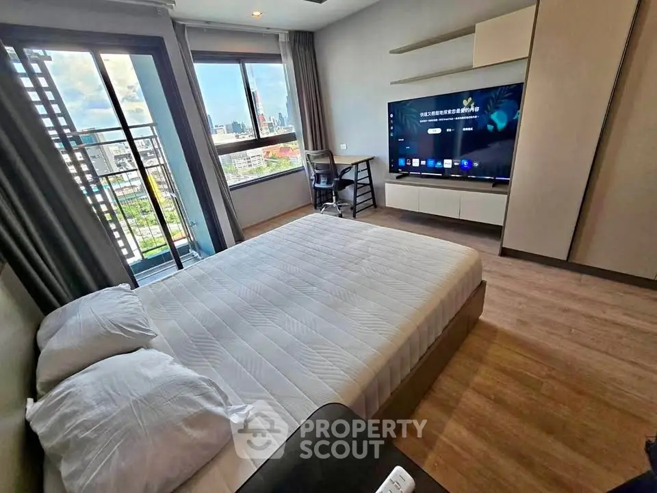 Modern bedroom with large window and city view, featuring a sleek TV and stylish furniture.