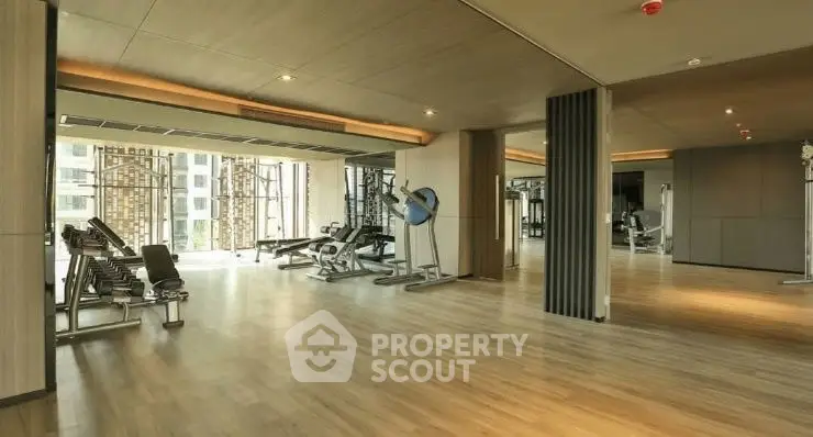 Spacious modern gym with state-of-the-art equipment and wooden flooring in luxury apartment complex.