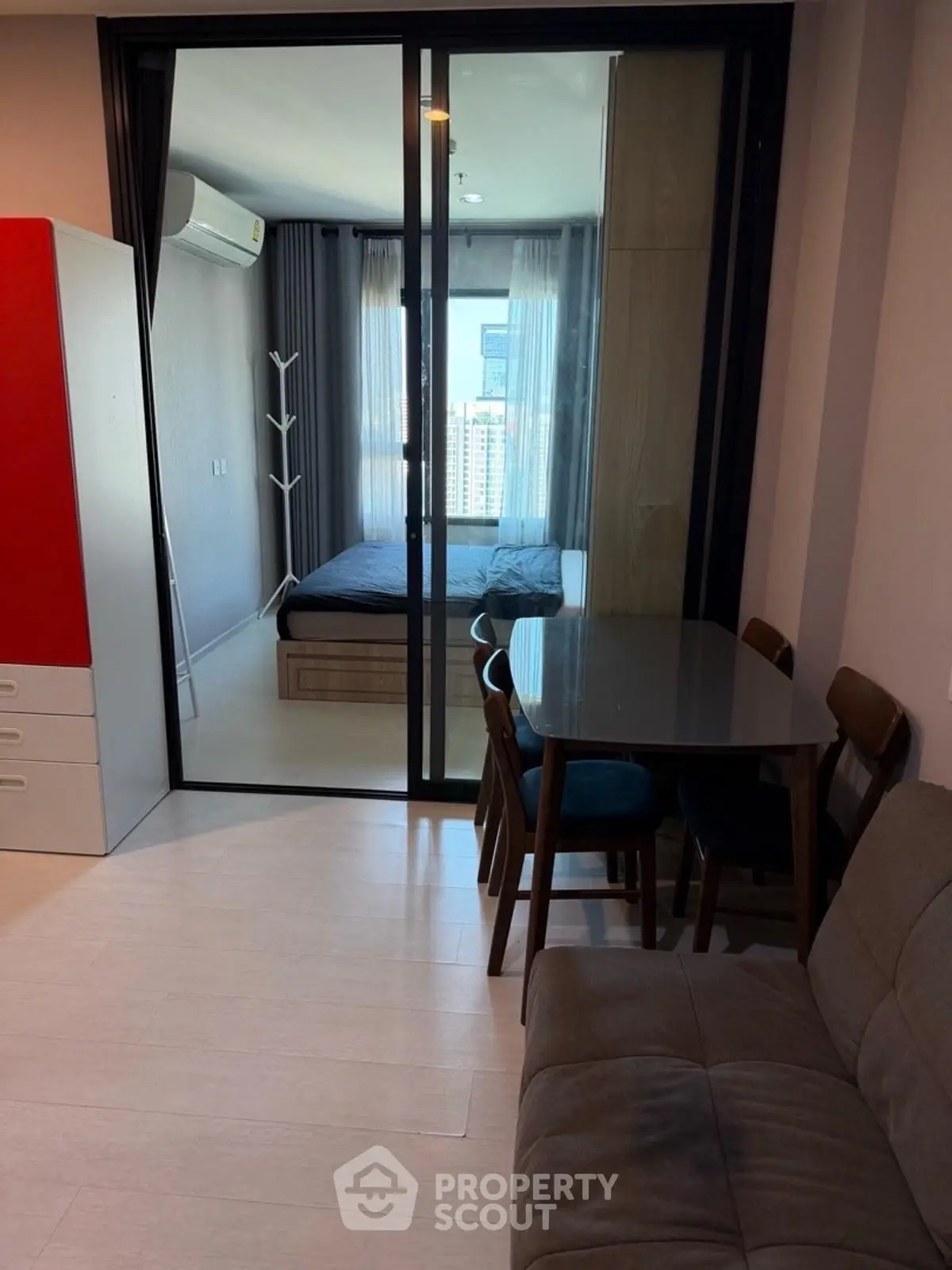 Modern apartment interior with glass sliding doors separating bedroom and living area, featuring sleek furniture.