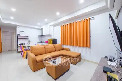 Modern living room with open kitchen, featuring cozy orange sofa and vibrant decor.