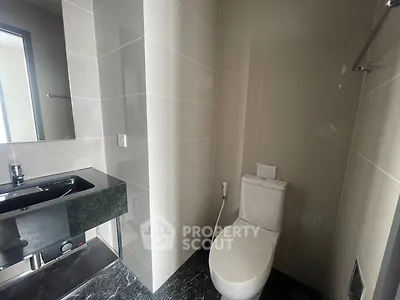 Modern bathroom with sleek black sink and white toilet in a compact space.