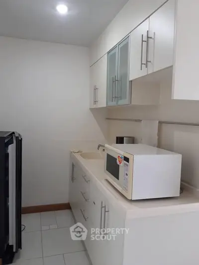 Modern kitchen with sleek white cabinets and microwave, perfect for compact living spaces.