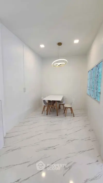 Modern dining area with sleek white table and chairs, elegant lighting, and marble flooring.