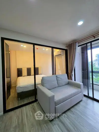 Modern apartment with glass-walled bedroom and cozy living area, featuring a large window with a scenic view.