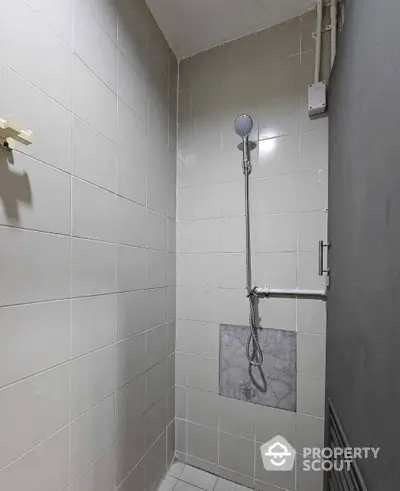 Compact modern bathroom with wall-mounted shower, pristine white tiles, and essential fixtures, perfect for urban living.