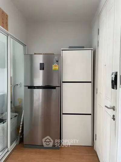 Modern kitchen corner with stainless steel fridge and sleek storage cabinet.