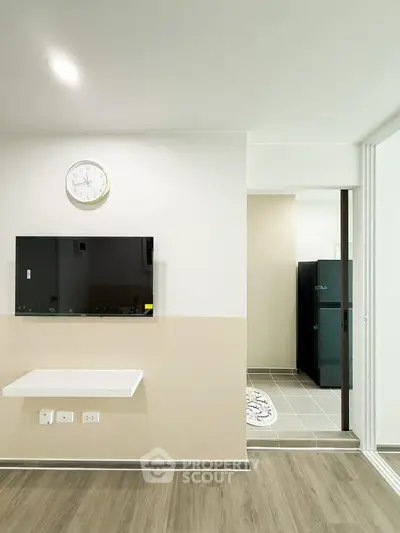 Modern interior with wall-mounted TV and clock, leading to a kitchen area with sleek appliances.