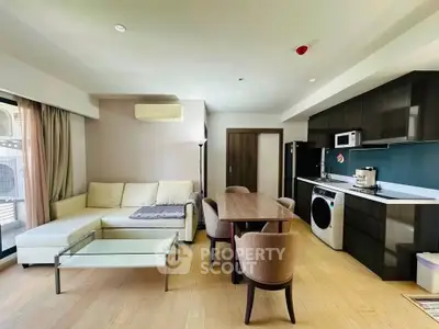 Modern open-layout living room with kitchen, featuring sleek furniture and appliances.