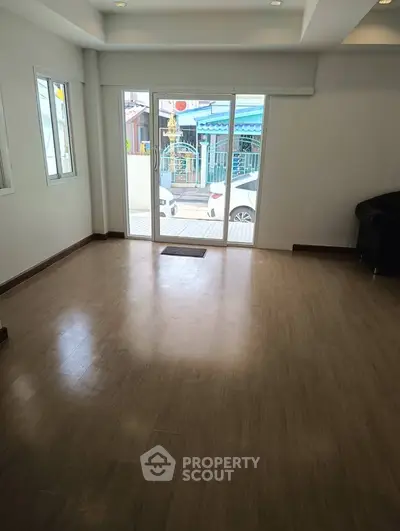 Spacious living room with wooden flooring and large windows offering natural light.
