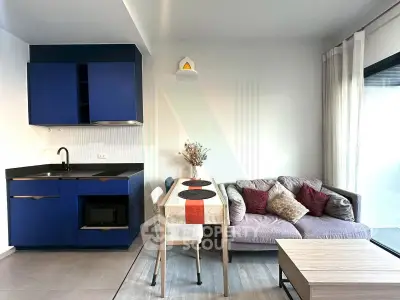Modern living room with compact kitchen and cozy dining area, featuring sleek blue cabinets and stylish decor.