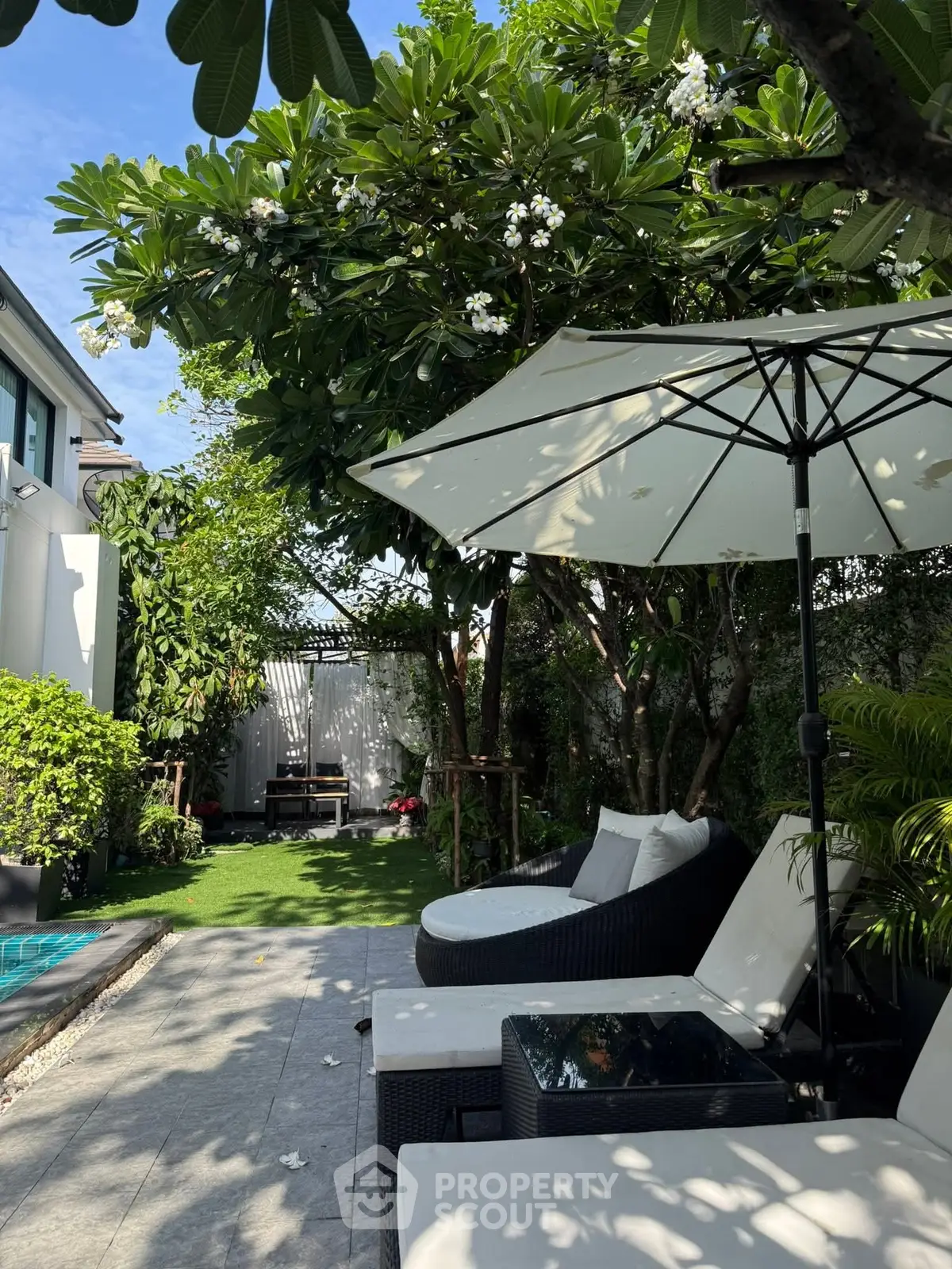 Luxurious garden with poolside lounge chairs and umbrella, perfect for relaxation.