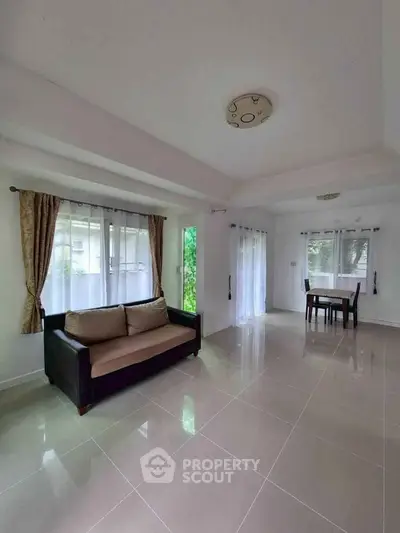 Spacious living room with modern sofa and dining area, featuring large windows and elegant curtains.
