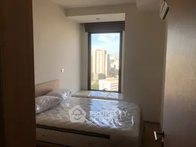 Cozy bedroom with city view, featuring a comfortable bed and large window for natural light.