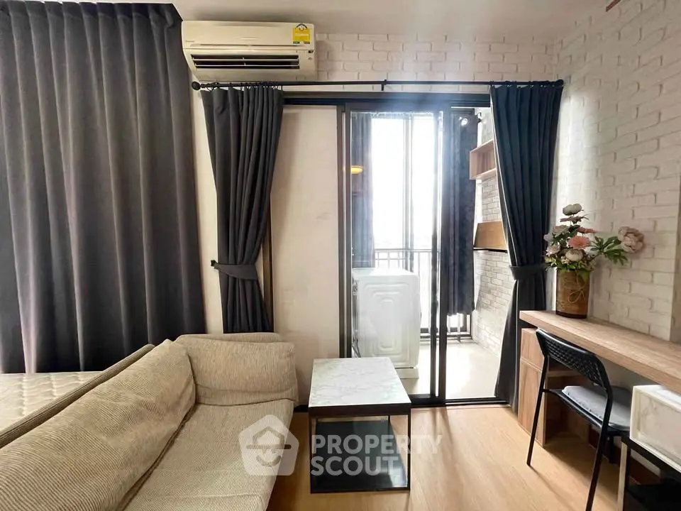 Modern living room with balcony access, featuring cozy sofa, desk, and washing machine for urban convenience.
