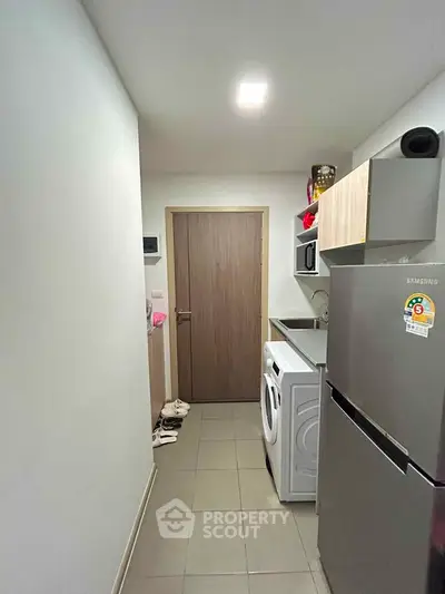 Compact kitchen with modern appliances including fridge and washing machine in a cozy apartment.