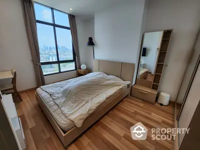 Spacious bedroom with large window offering city views, hardwood flooring, and modern furnishings, perfect for urban living.