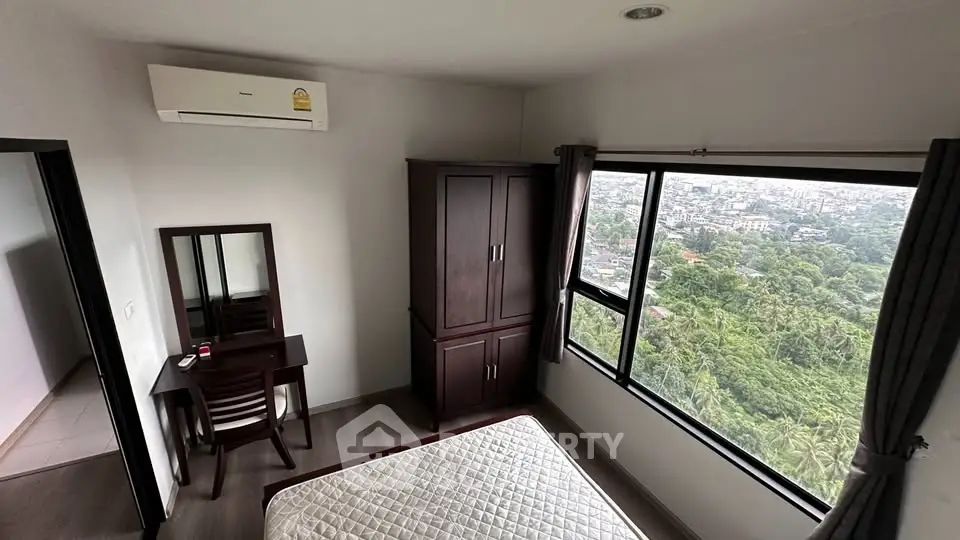 Spacious bedroom with large window offering stunning city and greenery views, featuring modern furniture and air conditioning.