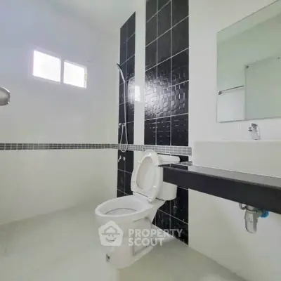 Modern bathroom with sleek black and white tiles, featuring a shower and contemporary fixtures.
