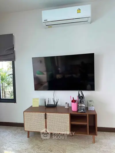 Modern living room with wall-mounted TV and stylish wooden cabinet under air conditioning unit.