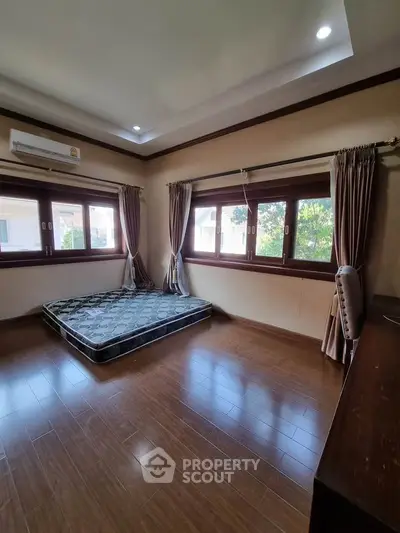 Spacious bedroom with wooden flooring and large windows for natural light.