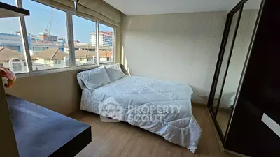 Cozy bedroom with large windows offering city views, featuring a comfortable bed and sleek mirrored wardrobe.