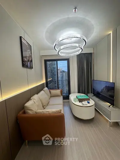 Modern living room with elegant chandelier and city view, featuring cozy sofa and sleek TV setup.