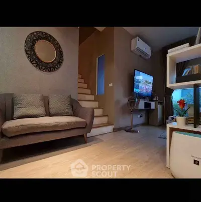 Modern living room with stylish decor and staircase, featuring a cozy sofa and wall-mounted TV.