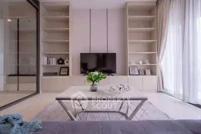 Modern living room with sleek built-in shelves and large TV, featuring elegant decor and natural light.
