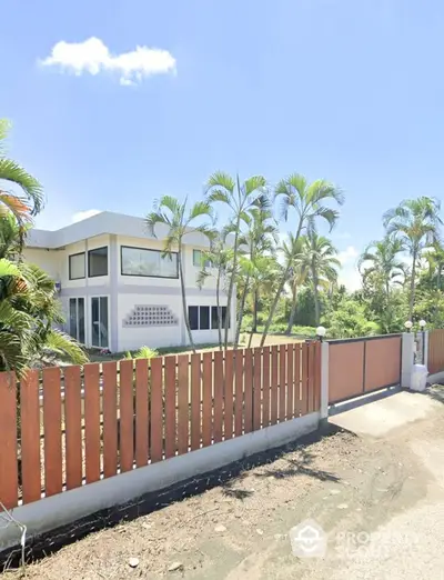 Modern tropical home with lush garden and wooden fence in serene neighborhood