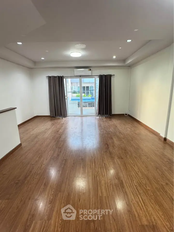 Spacious living room with wooden flooring and large windows offering natural light.