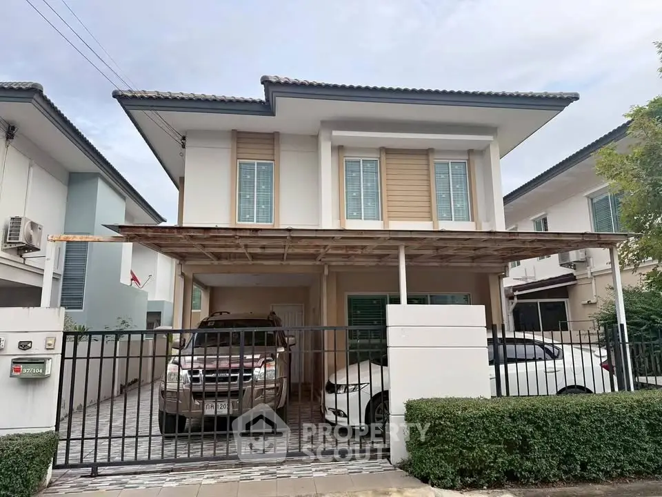 Modern two-story house with gated driveway and two cars parked in front.