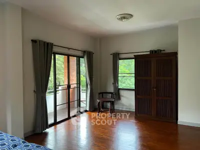 Spacious bedroom with wooden floors and balcony access in serene setting.