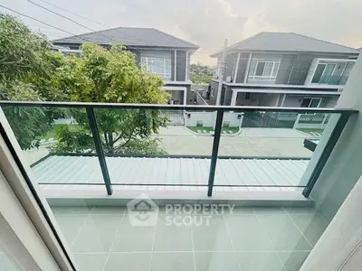 Modern balcony with glass railing overlooking suburban houses and greenery.