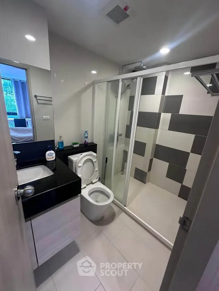 Modern bathroom with glass shower and sleek black countertop in contemporary apartment.