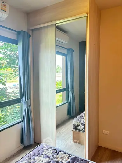 Cozy bedroom with mirrored wardrobe and large windows offering lush green views.