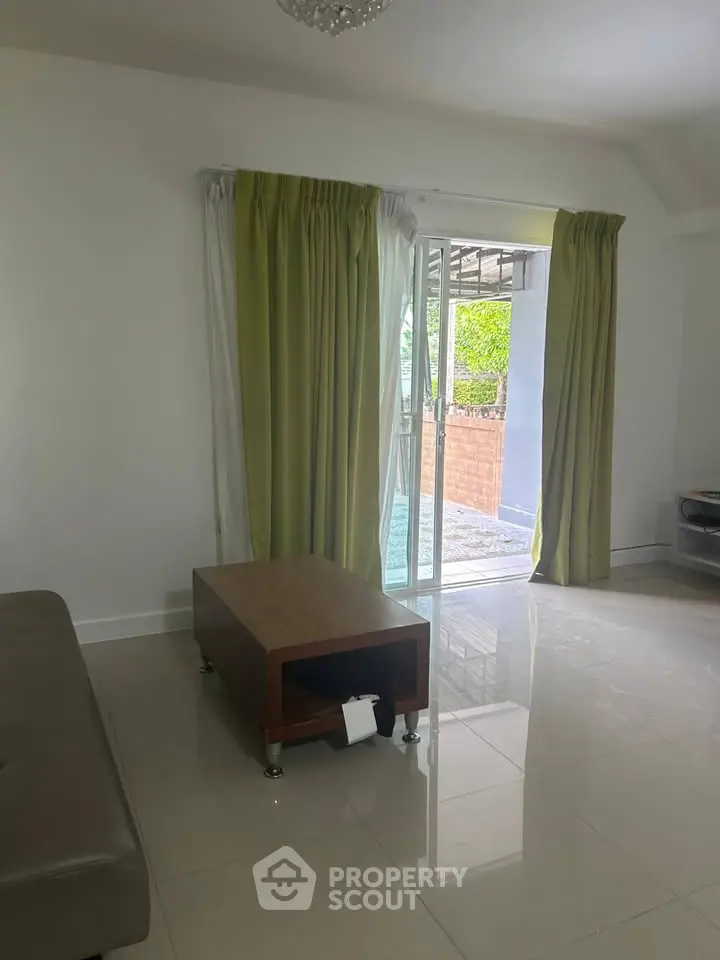 Spacious living room with sliding glass doors leading to a cozy balcony, featuring elegant green curtains.