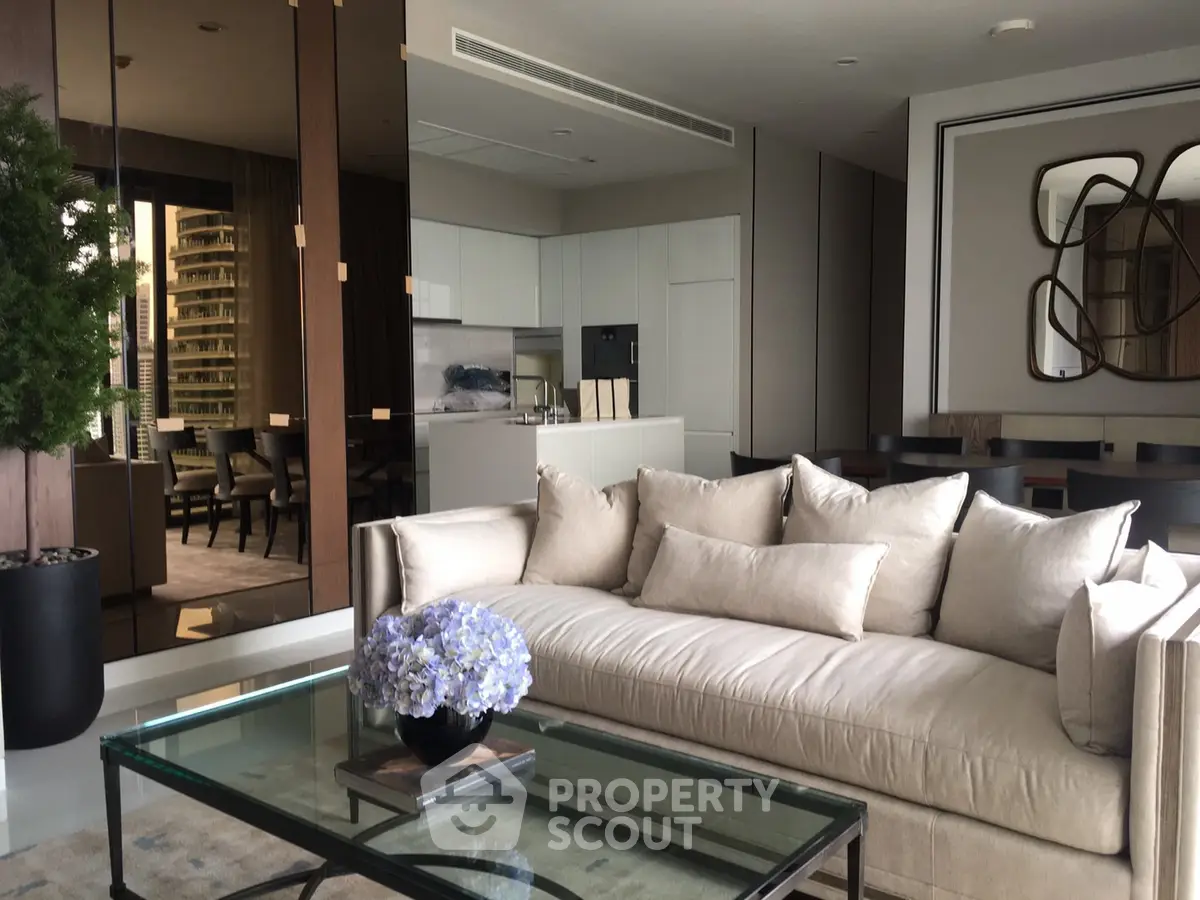 Luxurious modern living room with plush sofa and glass coffee table, open to elegant dining area.