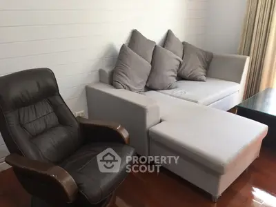 Cozy living room with modern gray sofa and leather armchair on wooden flooring.
