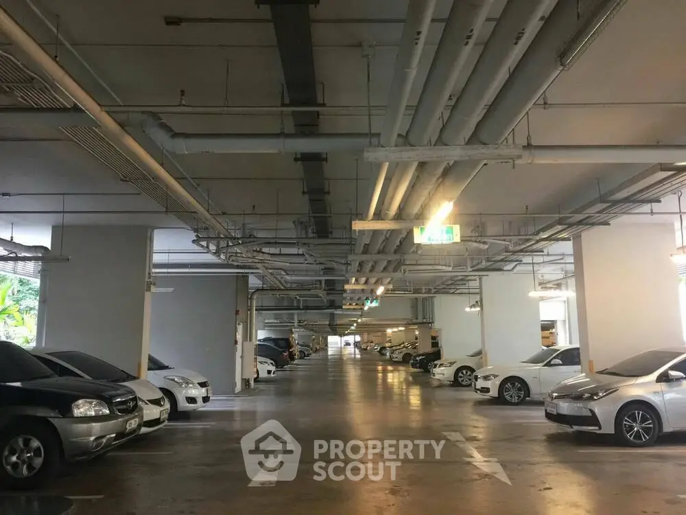 Spacious indoor parking area with multiple parked cars and overhead piping.