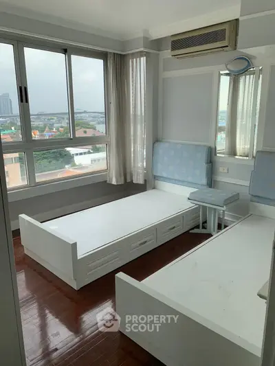 Bright bedroom with twin beds and large windows offering city views, featuring hardwood floors and air conditioning.
