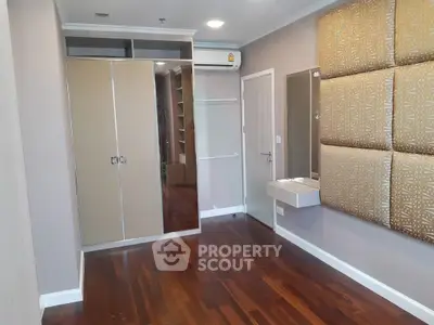 Spacious bedroom with wooden flooring and built-in wardrobe in modern apartment.