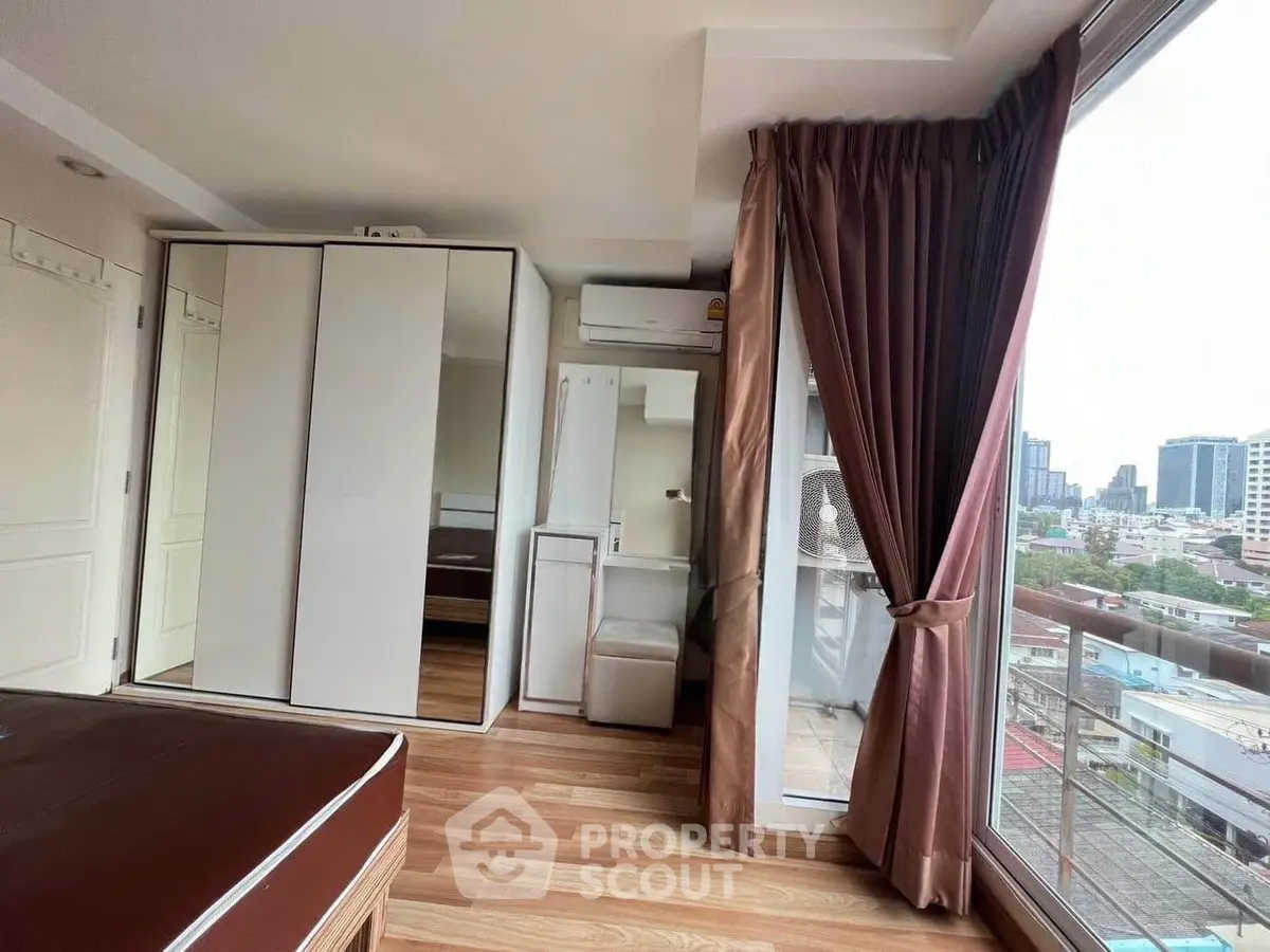 Modern bedroom with large windows and city view, featuring sleek wardrobe and wooden flooring.