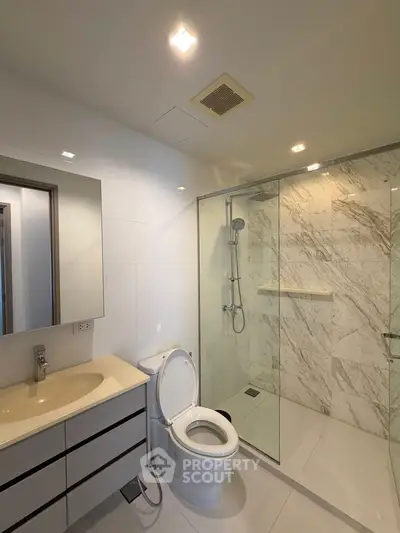 Modern bathroom with glass shower and sleek vanity in contemporary apartment.