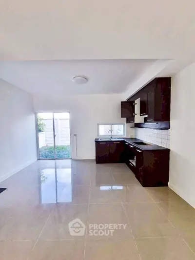 Modern open kitchen with sleek cabinetry and tiled flooring, leading to a bright outdoor space.