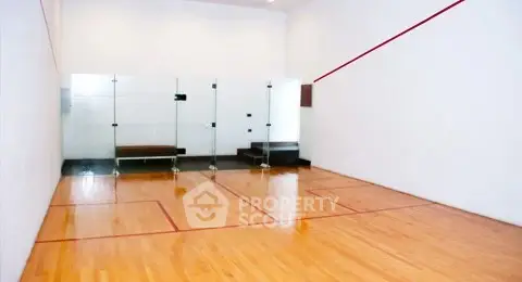 Spacious indoor squash court with wooden flooring and glass walls.